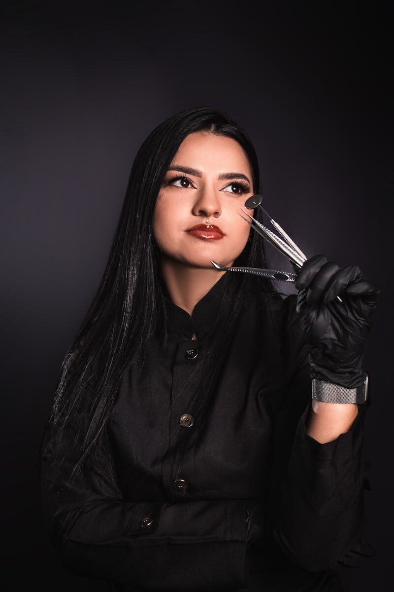 Portrait of a brunette woman in black gloves holding dental tools, captured in a studio setting.